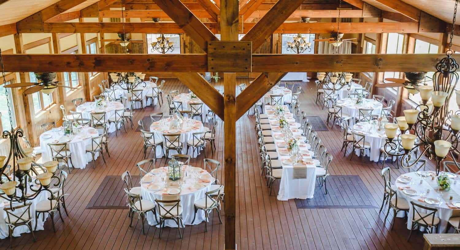 wedding venue set up with round tables with white tablecloths and metal chairs with wood floors and beams