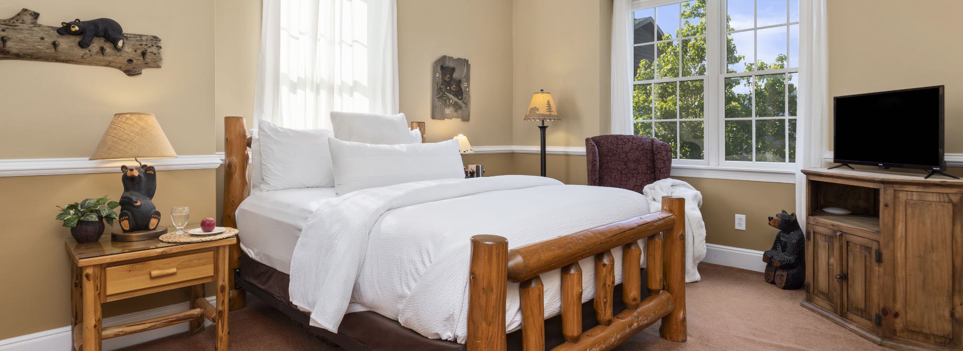 Bedroom with light tan walls, white trim, carpeting, log style bed, white bedding, and armchair