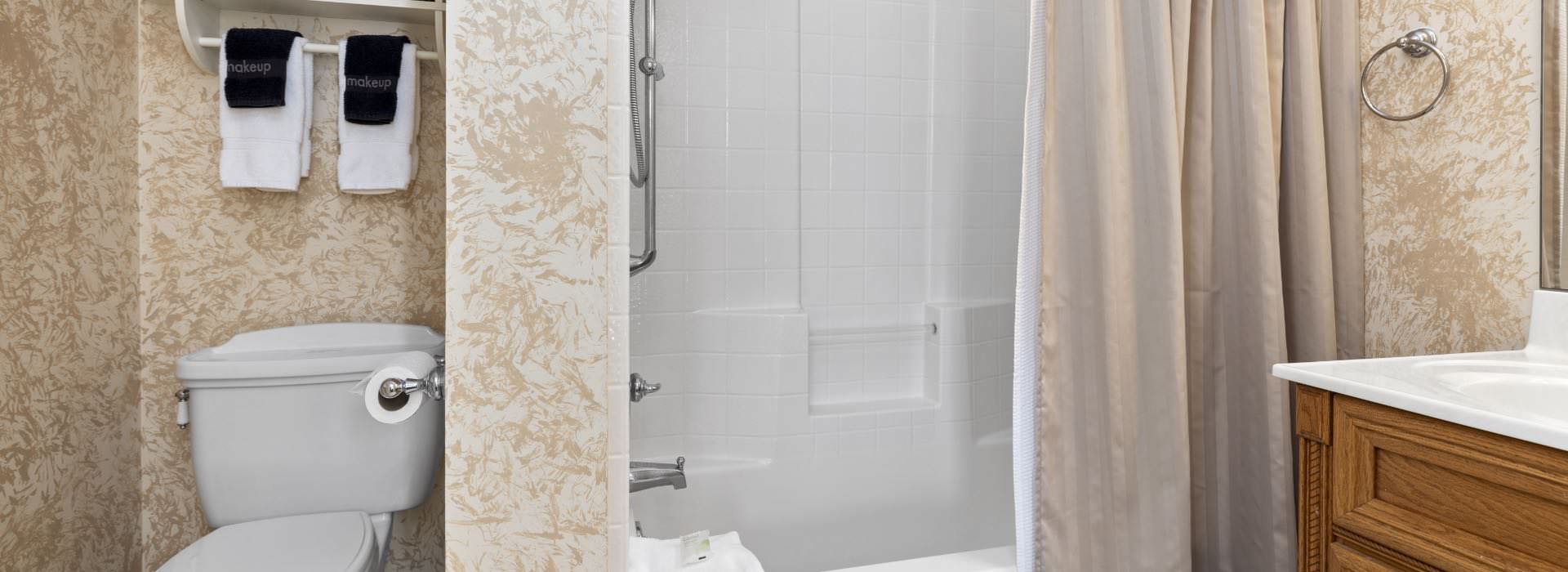 Bathroom with light colored wallpaper, shower/tub combo, and wooden vanity with white counter top