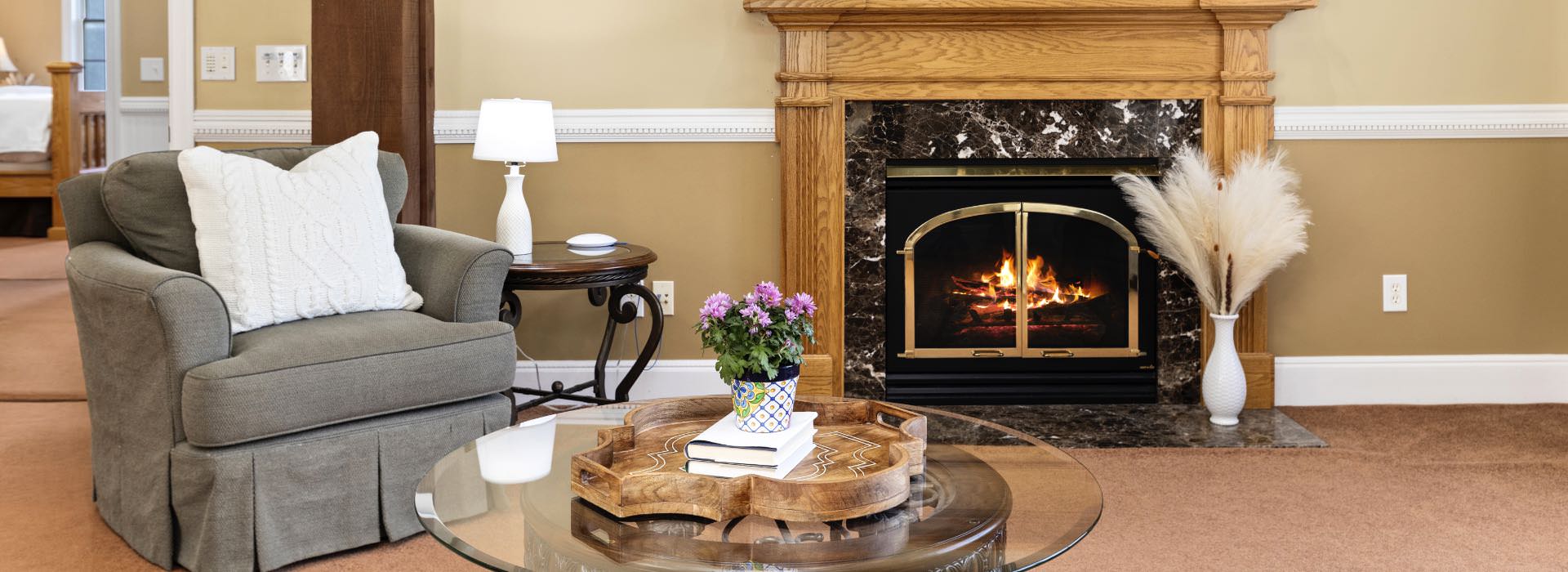 Sitting area in bedroom with gray upholstered chair, round glass table, and fireplace