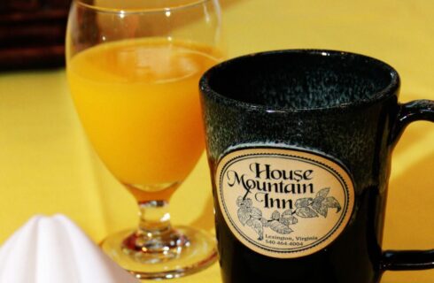 white napkin on a yellow tablecloth with a stoneware mug with House Mountain Inn logo and a glass of orange juice