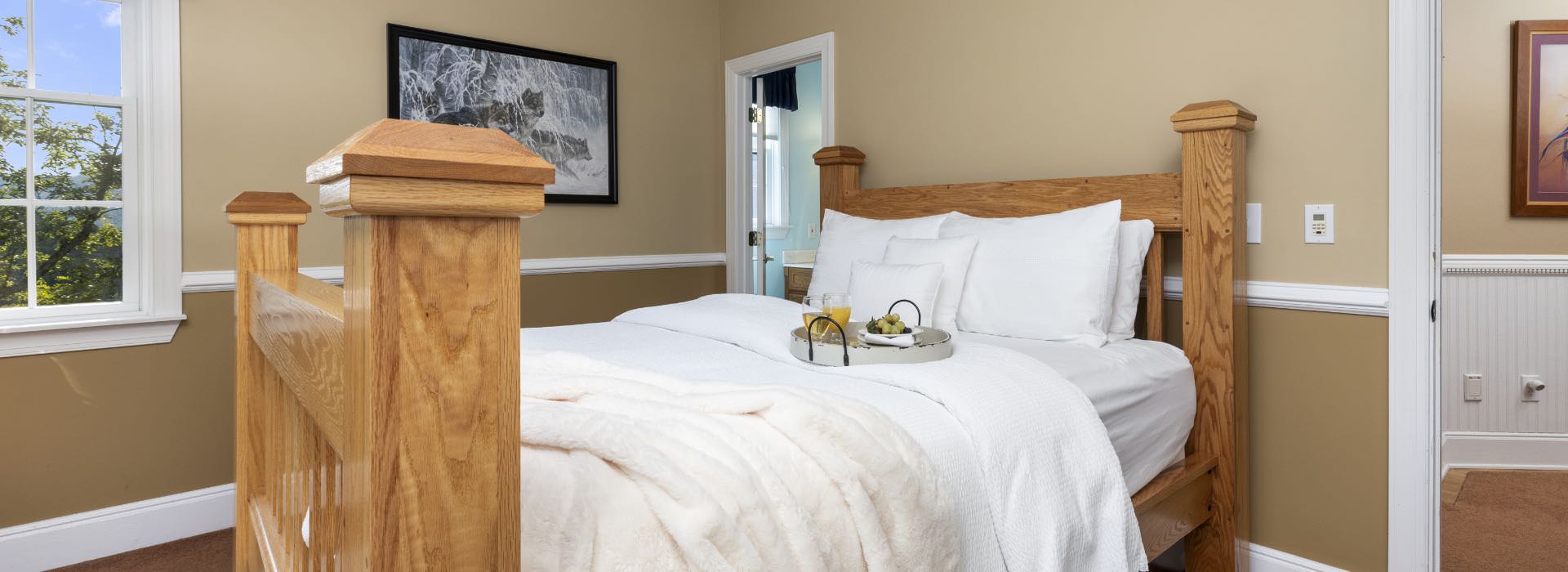 Bedroom with light tan walls, white trim, carpeting, large wooden bed, and white bedding