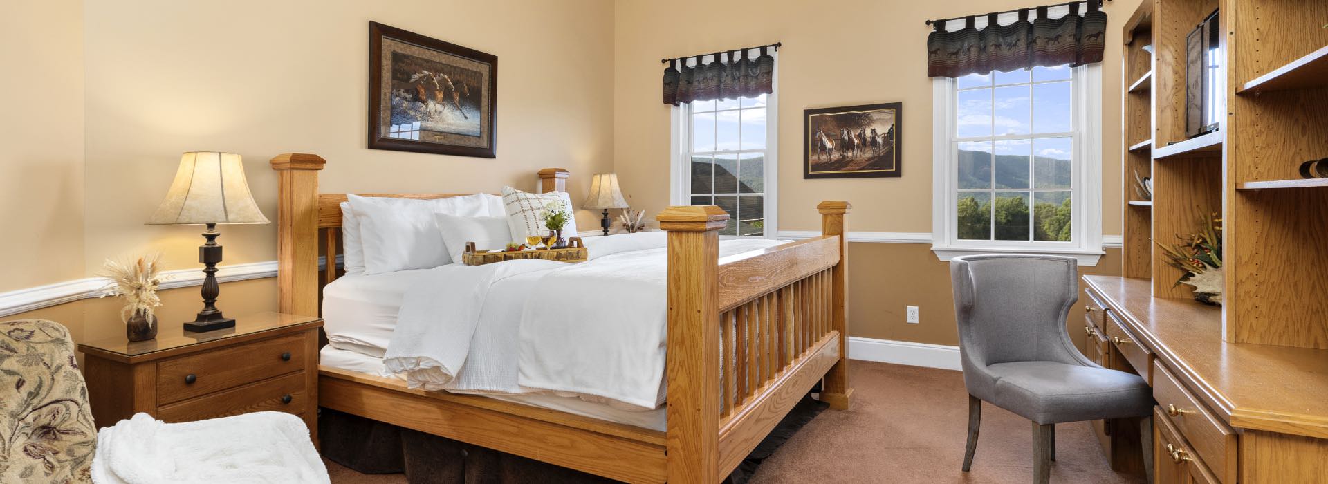 Bedroom with light tan walls, white trim, carpeting, large wooden bed, white bedding, and built in desk and shelving