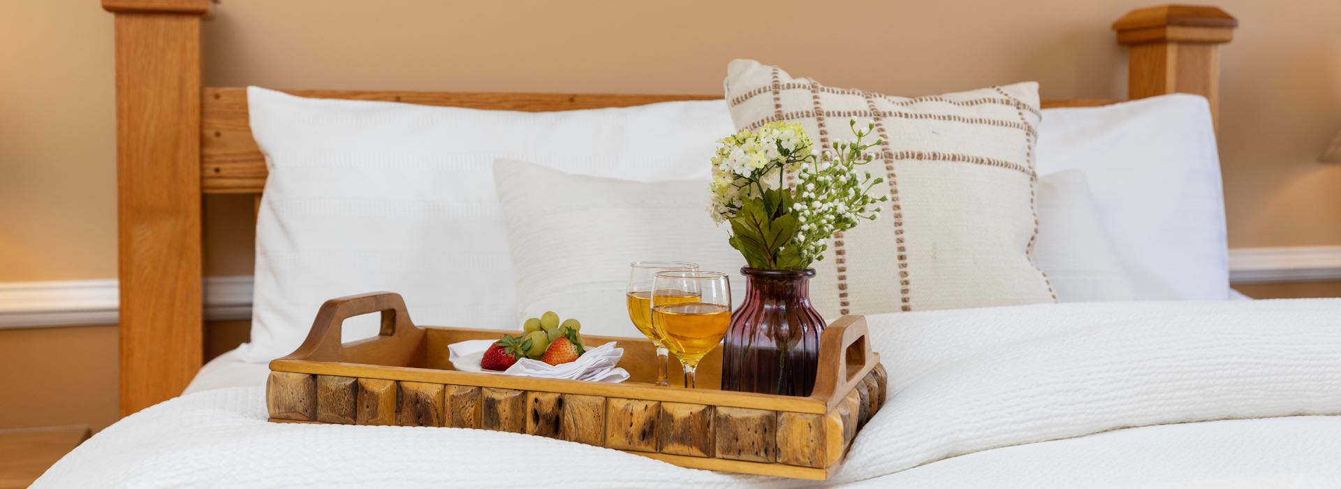 Close up view of tray with two glasses of apple juice, small vase with white flower, and small plate of fruit