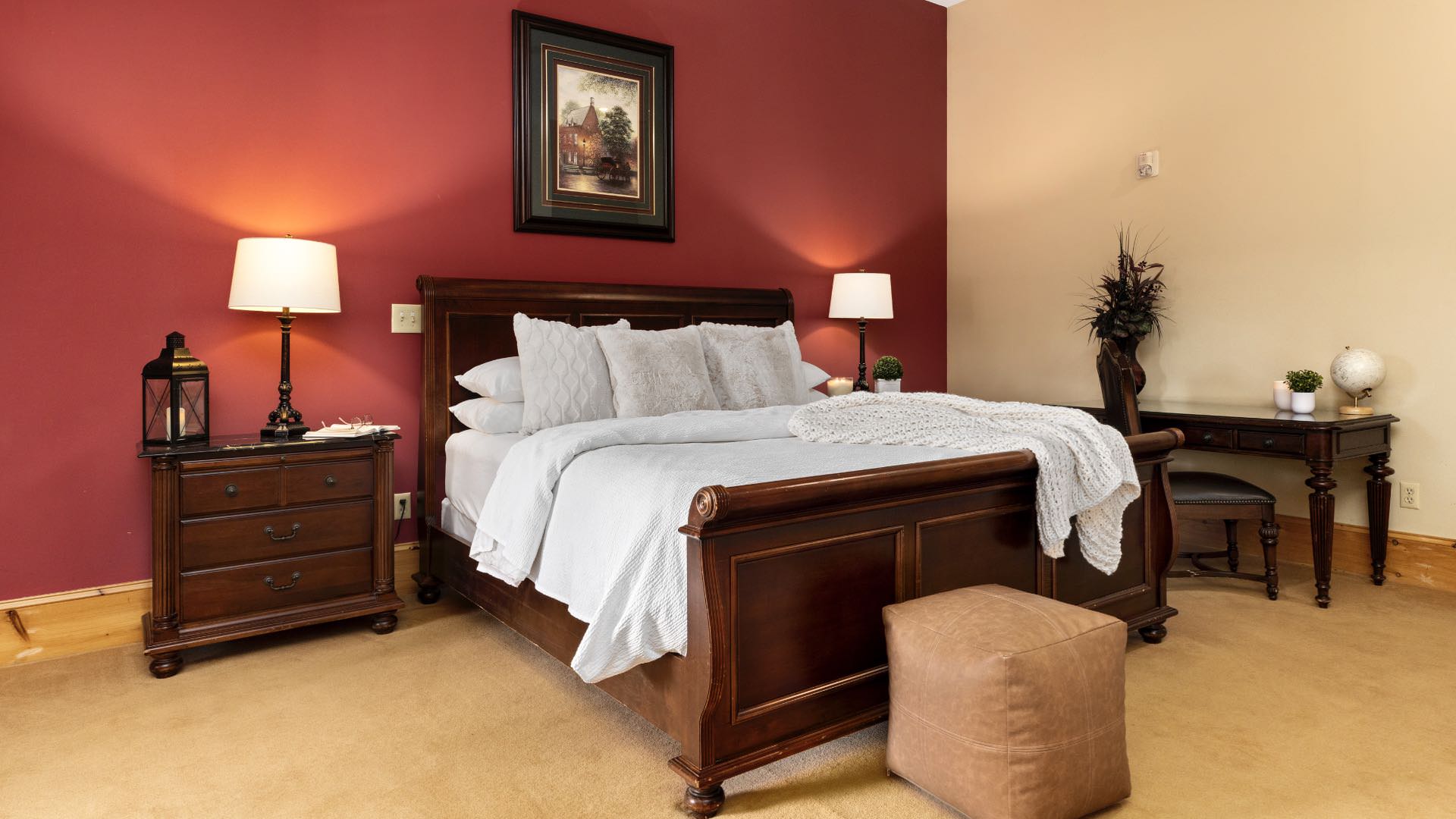 Bedroom with cream and red walls, wood trim, carpeting, dark wooden sleigh bed, white bedding, and dark wooden nightstand and desk