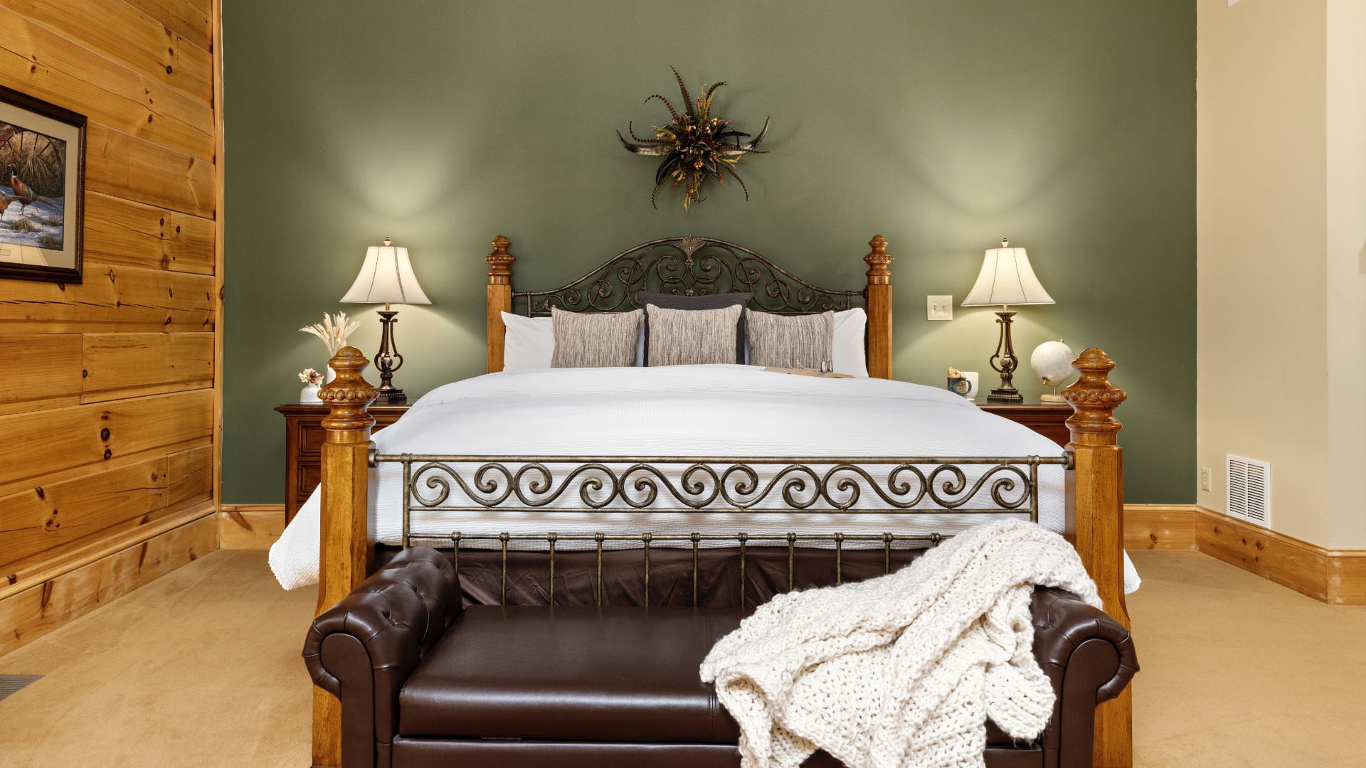 Bedroom with sage green and wood paneled walls, wood trim, carpeting, wooden four-poster bed, white bedding, and dark leather chaise