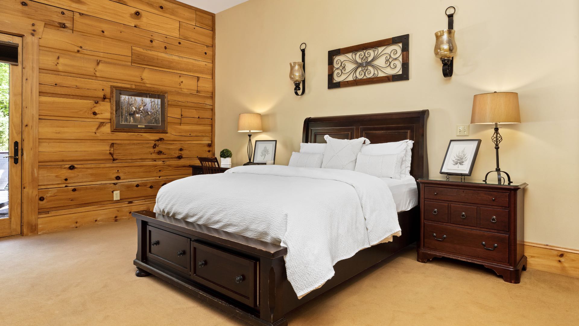 Bedroom with cream and wood paneled walls, wood trim, carpeting, wooden bed, white bedding, and dark wooden nightstand and desk