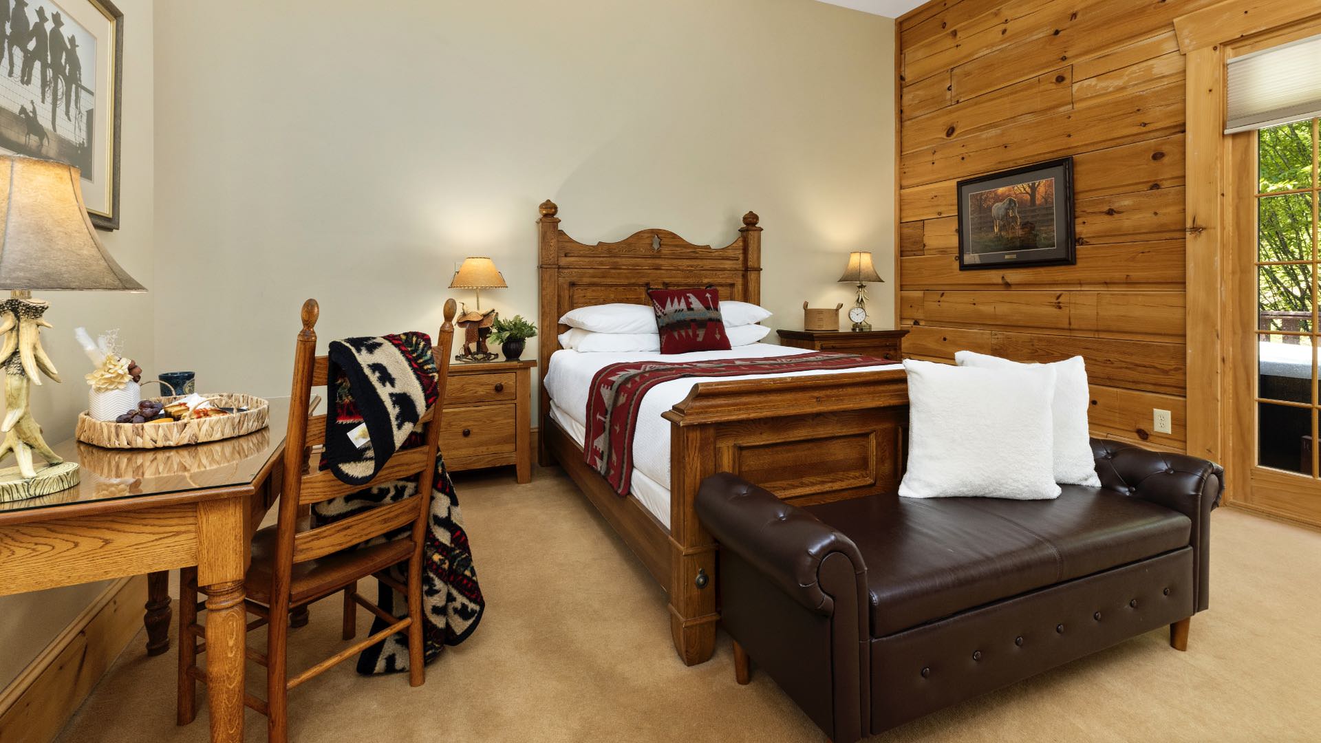 Bedroom with cream and wood paneled walls, wood trim, carpeting, wooden bed, white bedding, dark leather chaise, and wooden nightstands and desk
