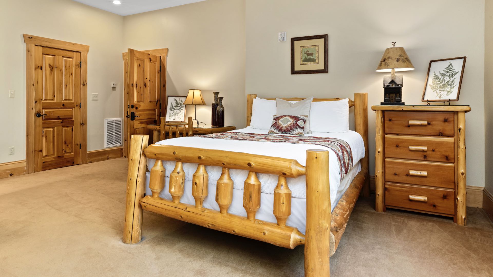 Bedroom with cream walls, wood trim, carpeting, wooden log bed, white bedding, and matching nightstand and desk