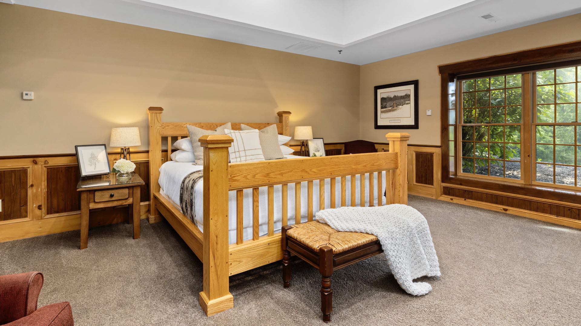 Bedroom with cream walls, wood trim, carpeting, wooden four-poster bed, white bedding, and large windows
