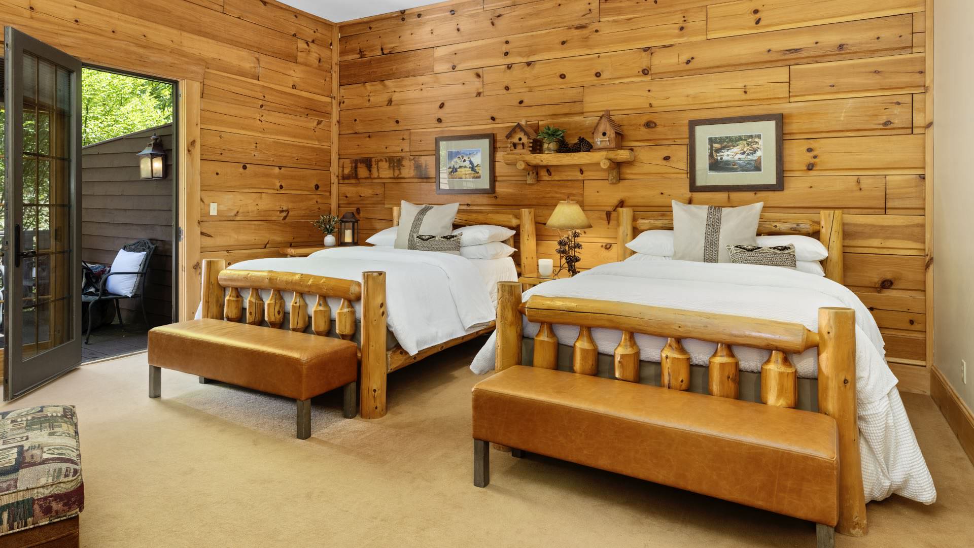Bedroom with wood paneled walls, wood trim, carpeting, two wooden log beds, white bedding, and door to deck