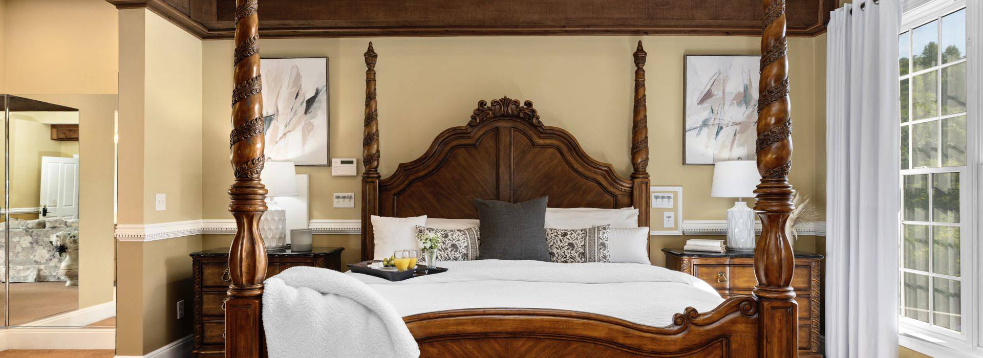 Bedroom with light tan walls, white trim, carpeting, wooden four-poster bed, white bedding, and wooden nightstands