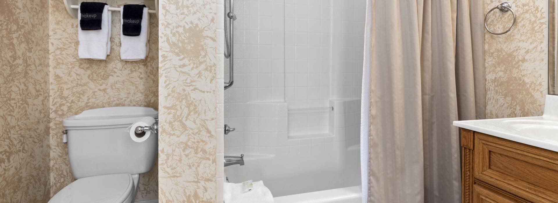 Bathroom with light colored wallpaper, shower/tub combo, and wooden vanity with white counter top